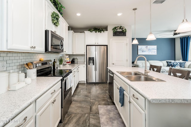 kitchen featuring appliances with stainless steel finishes, a sink, stone finish floors, tasteful backsplash, and open floor plan