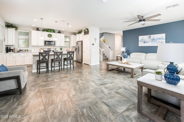 living area with stairway, ceiling fan, and baseboards