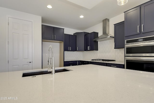 kitchen with wall chimney range hood, sink, appliances with stainless steel finishes, light stone counters, and decorative backsplash