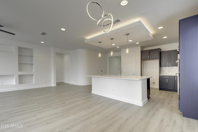 kitchen featuring decorative light fixtures, light hardwood / wood-style flooring, an island with sink, built in features, and backsplash