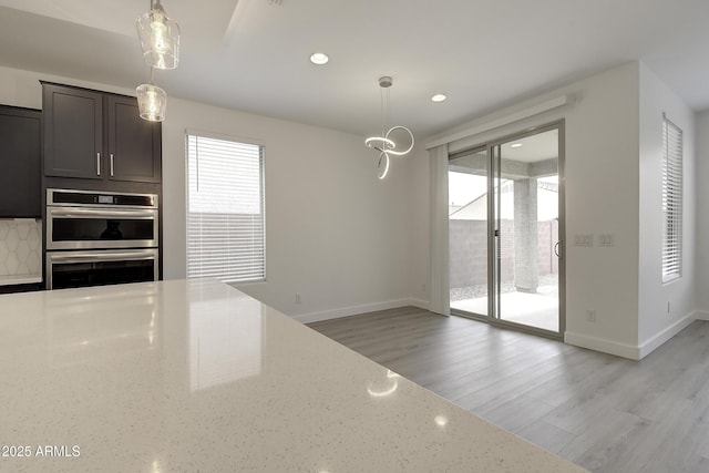 kitchen with light stone counters, hanging light fixtures, light hardwood / wood-style flooring, and stainless steel double oven