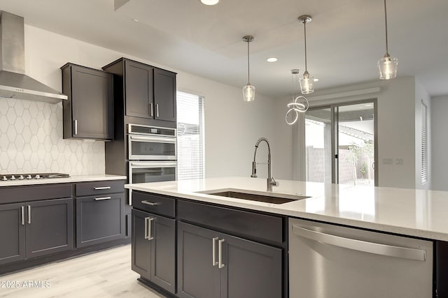 kitchen with appliances with stainless steel finishes, decorative light fixtures, sink, a healthy amount of sunlight, and wall chimney exhaust hood