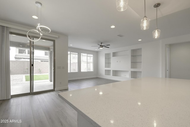 unfurnished living room with built in shelves, ceiling fan, and hardwood / wood-style flooring