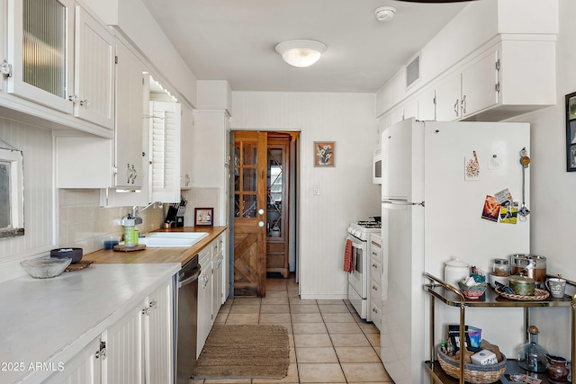 kitchen featuring white appliances, light countertops, white cabinets, a sink, and light tile patterned flooring