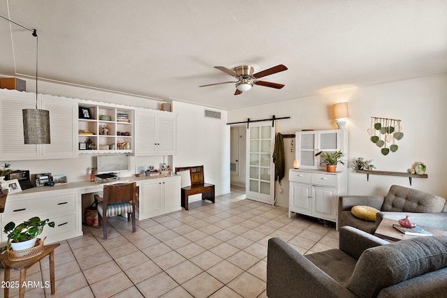 living area with a barn door, light tile patterned floors, ceiling fan, visible vents, and built in study area