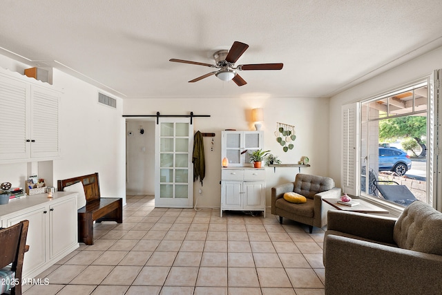 living area with visible vents, a barn door, a ceiling fan, and light tile patterned flooring