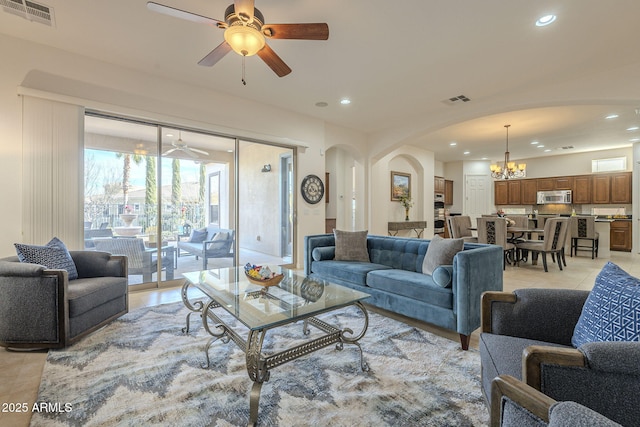 tiled living room with ceiling fan with notable chandelier