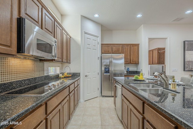 kitchen featuring sink, light tile patterned floors, dark stone countertops, stainless steel appliances, and decorative backsplash