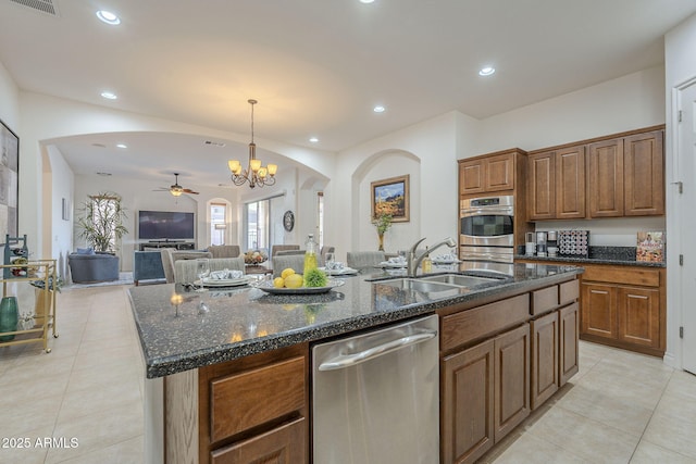 kitchen featuring sink, dark stone countertops, stainless steel appliances, a center island with sink, and decorative light fixtures