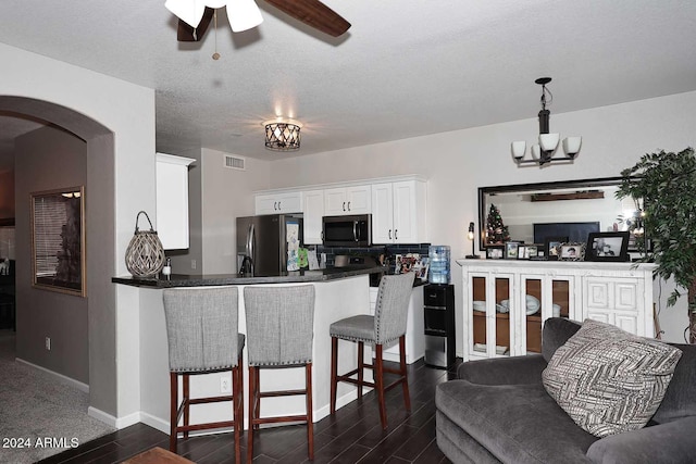 kitchen with kitchen peninsula, stainless steel fridge, a textured ceiling, a kitchen bar, and white cabinetry