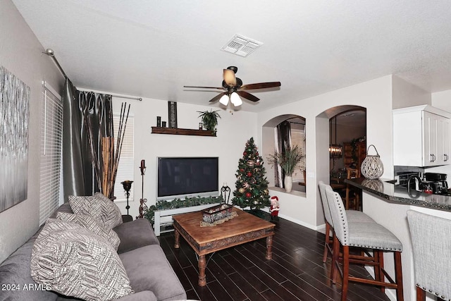 living room featuring ceiling fan, dark wood-type flooring, and a textured ceiling