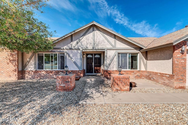 entrance to property featuring brick siding, a patio area, and stucco siding