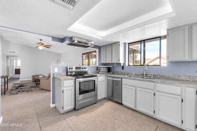 kitchen featuring stainless steel appliances, a tray ceiling, light countertops, and a sink