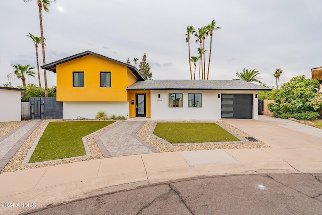 tri-level home featuring a garage, concrete driveway, a front lawn, and stucco siding