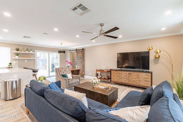 living room with ornamental molding, visible vents, light wood finished floors, and a barn door