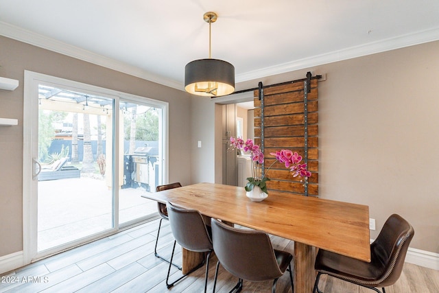 dining area featuring ornamental molding, a barn door, light wood-type flooring, and baseboards