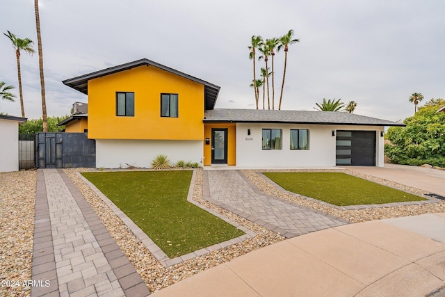 tri-level home featuring a garage, concrete driveway, a front yard, and stucco siding