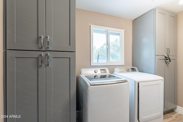 laundry area with light wood-type flooring, cabinet space, washing machine and dryer, and baseboards