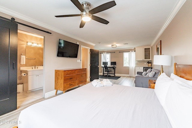 bedroom with light wood finished floors, a barn door, ornamental molding, ensuite bath, and baseboards