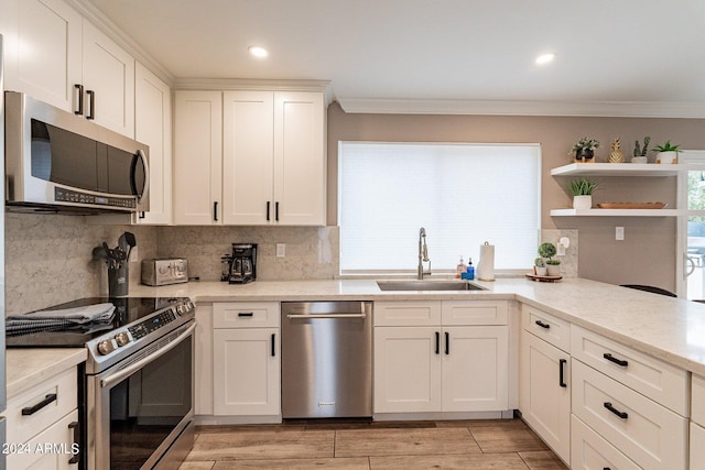 kitchen with light stone countertops, stainless steel appliances, crown molding, white cabinetry, and a sink