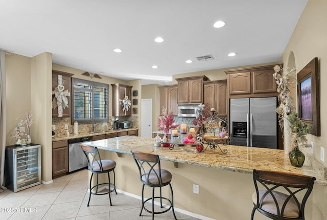 kitchen with light tile patterned floors, appliances with stainless steel finishes, a kitchen breakfast bar, light stone countertops, and backsplash