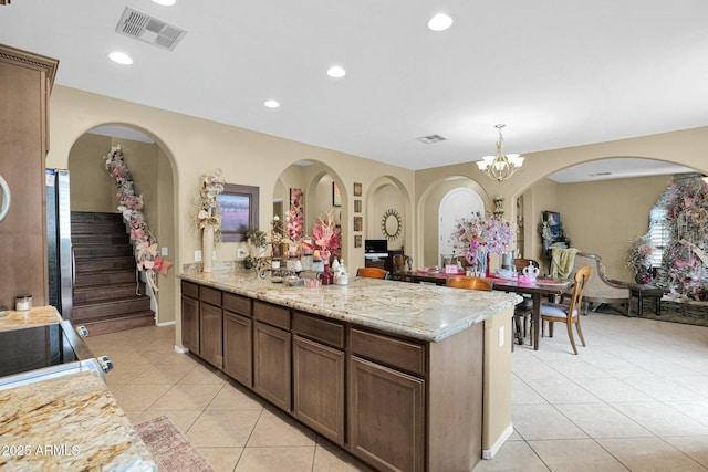 kitchen featuring a chandelier, light tile patterned floors, stainless steel fridge, pendant lighting, and light stone countertops