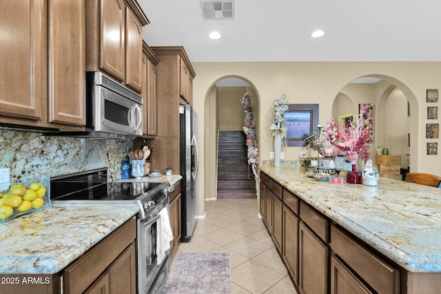 kitchen with light tile patterned flooring, a breakfast bar, light stone counters, appliances with stainless steel finishes, and backsplash