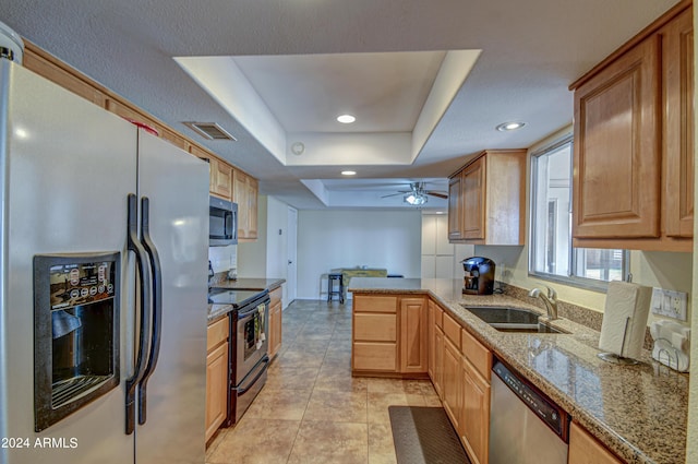 kitchen with sink, appliances with stainless steel finishes, a raised ceiling, kitchen peninsula, and light stone countertops