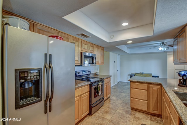 kitchen featuring stone counters, light tile patterned flooring, appliances with stainless steel finishes, ceiling fan, and a tray ceiling