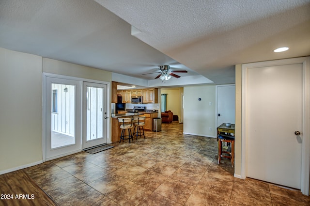 interior space with stainless steel appliances, ceiling fan, a breakfast bar area, and a textured ceiling