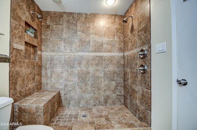 bathroom with toilet, a textured ceiling, and a tile shower