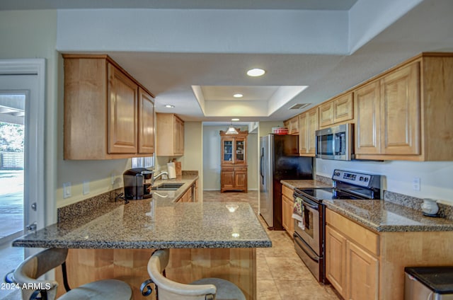 kitchen featuring a breakfast bar, appliances with stainless steel finishes, kitchen peninsula, a raised ceiling, and stone counters