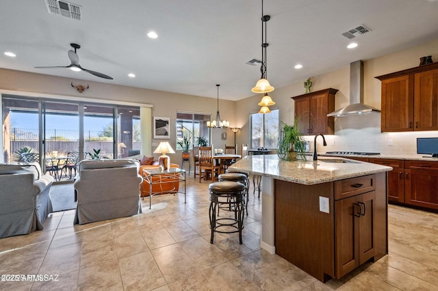 kitchen with visible vents, backsplash, open floor plan, wall chimney exhaust hood, and a sink