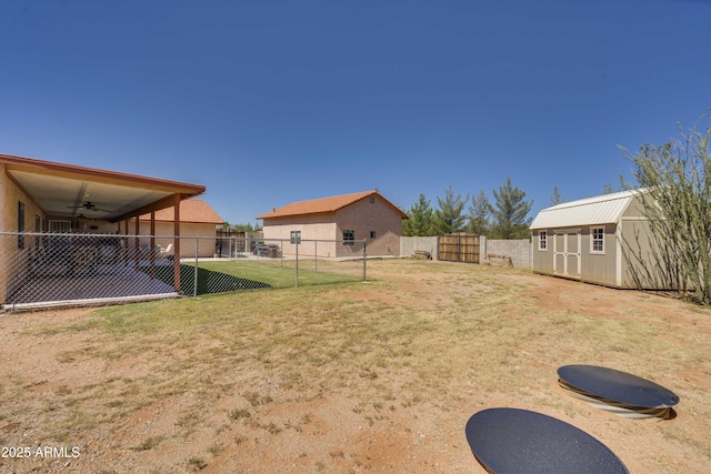 view of yard with an outdoor structure, a fenced backyard, ceiling fan, and a shed