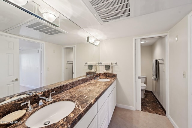 bathroom with a sink, baseboards, toilet, and double vanity