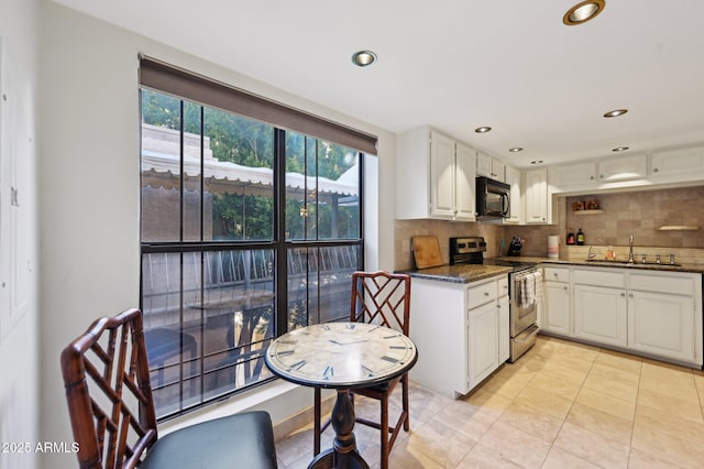 kitchen with decorative backsplash, black microwave, stainless steel range with electric stovetop, light tile patterned floors, and a sink