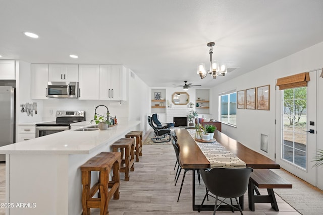 dining room featuring visible vents, ceiling fan with notable chandelier, light wood-style floors, a fireplace, and recessed lighting