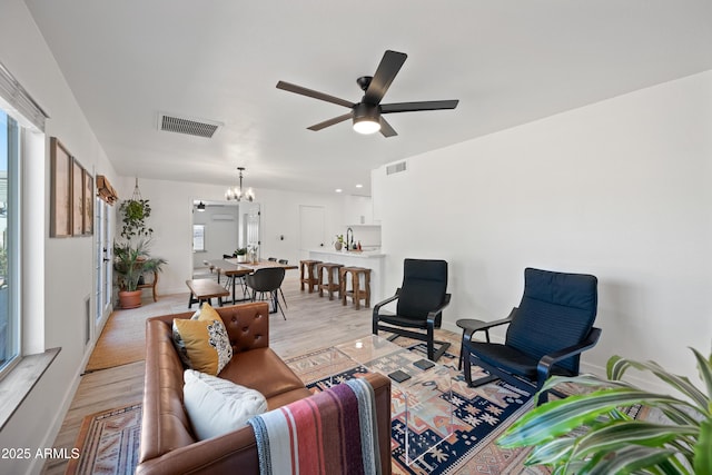 living area with visible vents, light wood finished floors, and ceiling fan with notable chandelier