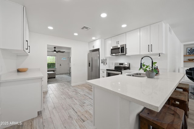 kitchen with light stone counters, stainless steel appliances, a peninsula, a sink, and visible vents