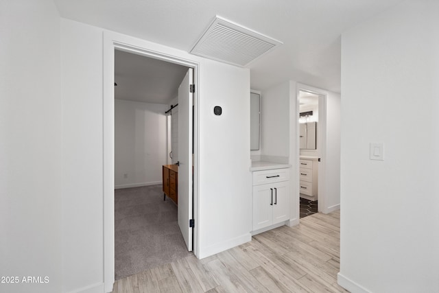 hall with light wood-type flooring, baseboards, visible vents, and a barn door