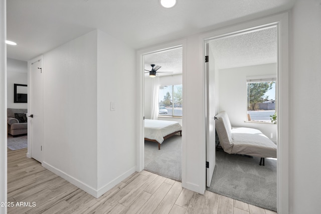 corridor featuring baseboards, a textured ceiling, and light wood finished floors