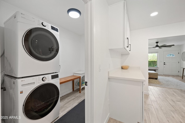 washroom featuring stacked washer and dryer, cabinet space, wood tiled floor, ceiling fan, and baseboards