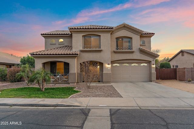 mediterranean / spanish house with driveway, a tile roof, an attached garage, fence, and stucco siding