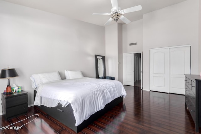 bedroom featuring a closet, dark hardwood / wood-style floors, ceiling fan, and a high ceiling