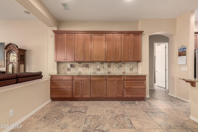 4615 S Primrose Dr, Gold Canyon, AZ 85118 - kitchen with arched walkways, brown cabinetry, backsplash, and light stone counters