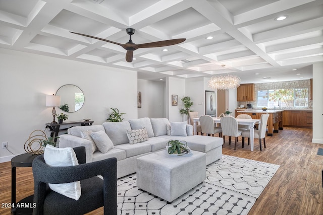 living room featuring ceiling fan with notable chandelier, coffered ceiling, light hardwood / wood-style floors, and beam ceiling