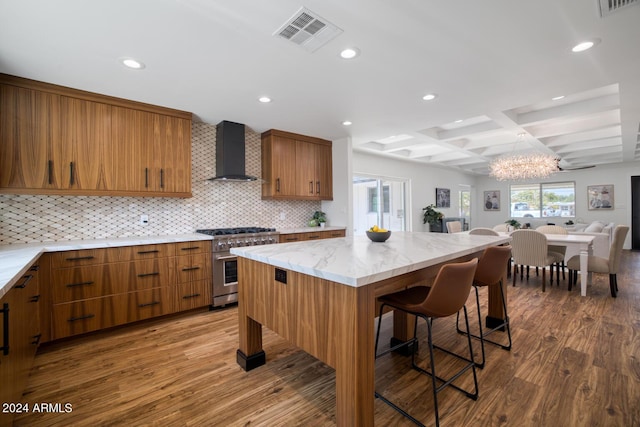 kitchen with a breakfast bar, high end stainless steel range oven, wall chimney exhaust hood, coffered ceiling, and beamed ceiling