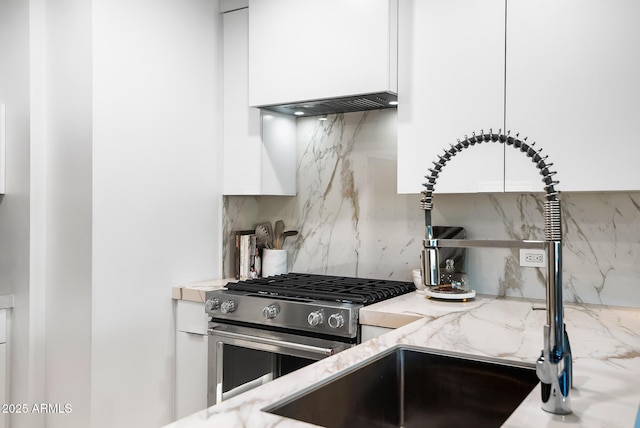 kitchen with tasteful backsplash, sink, white cabinets, light stone countertops, and stainless steel gas range