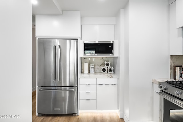 kitchen featuring white cabinetry, stainless steel appliances, light stone counters, tasteful backsplash, and light hardwood / wood-style floors