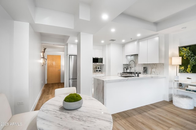 kitchen with sink, white cabinets, kitchen peninsula, stainless steel appliances, and light hardwood / wood-style flooring